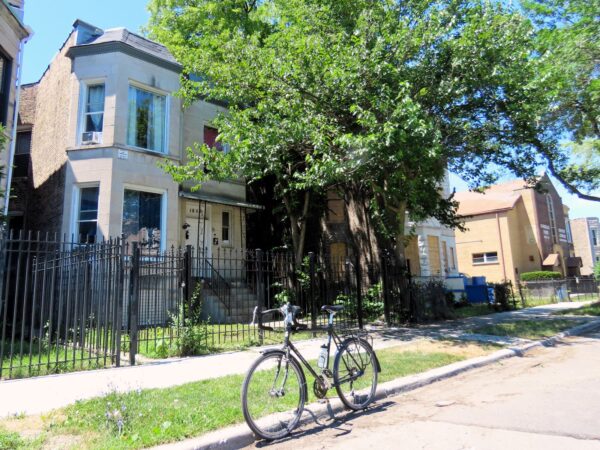 A tour bicycle standing in front of an early 1900s limestone two flat.