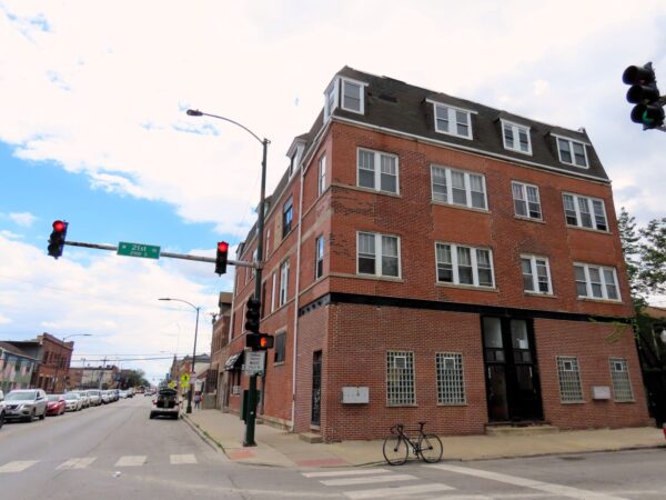 A tour bicycle standing at front of a row of late 1800s double lot four story corner apartment building.