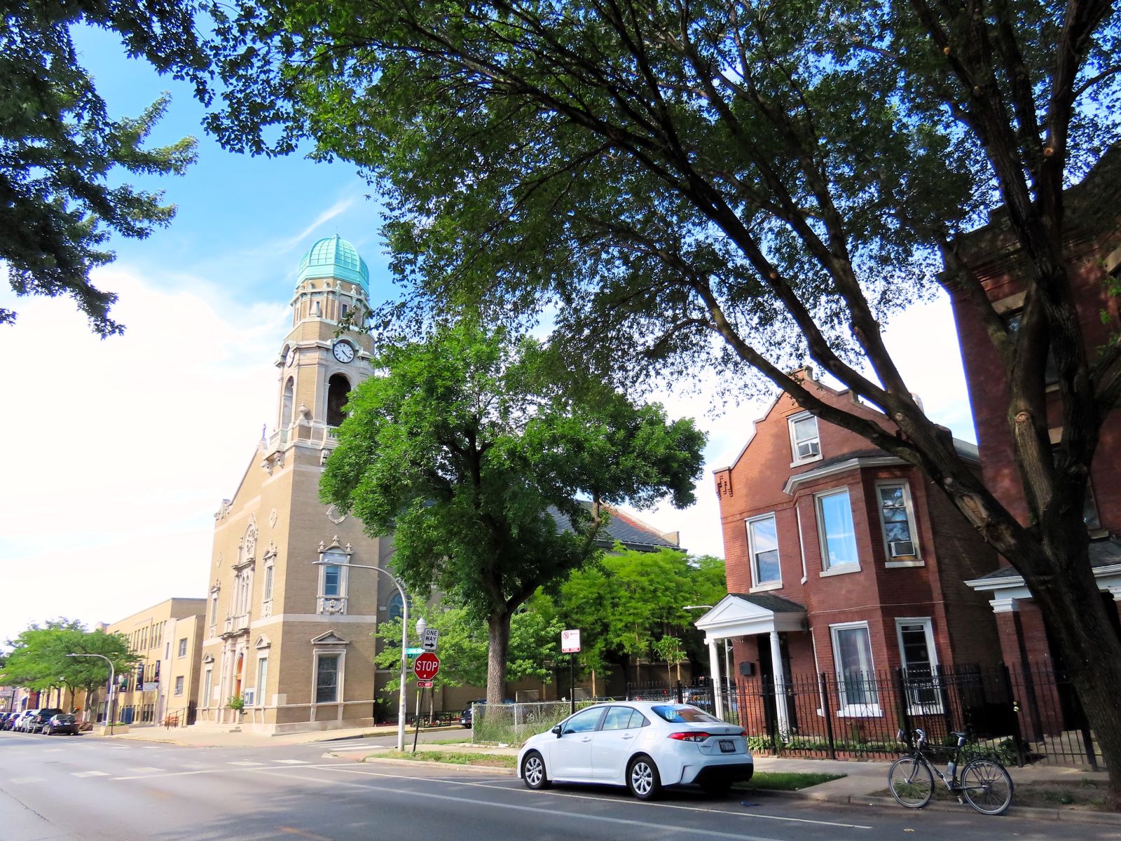 A tour bicycle standing in front of an early 1900s two story brick home with a looming Romanesque Revival yellow brick church down he street at left.