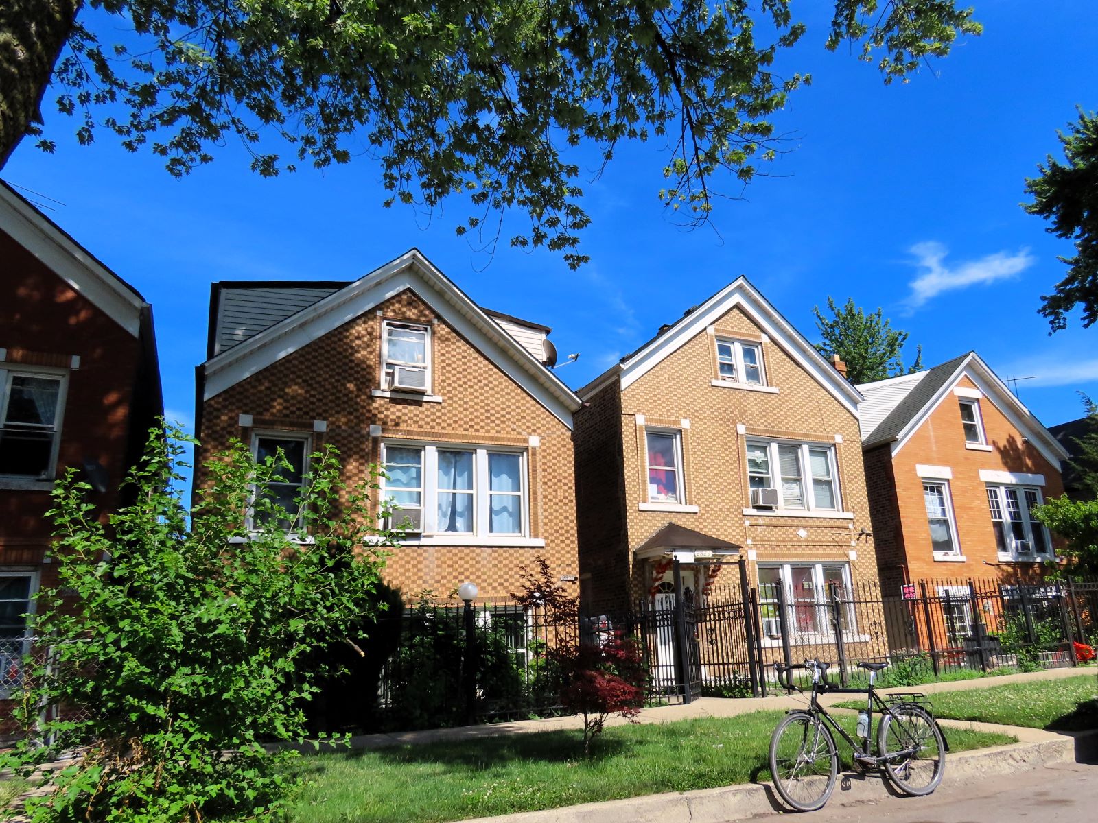 A tour bicycle standing in front of three early 1900s brick two story single family homes.