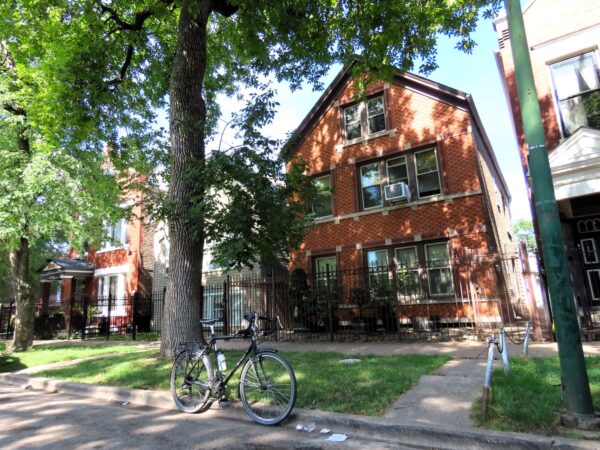 A tour bicycle standing in front of an early 1900s brick two story single family home under tree shade.