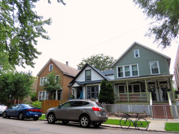 On a neighborhood street a tour bicycle is standing at front of early 1900s wood frame homes.