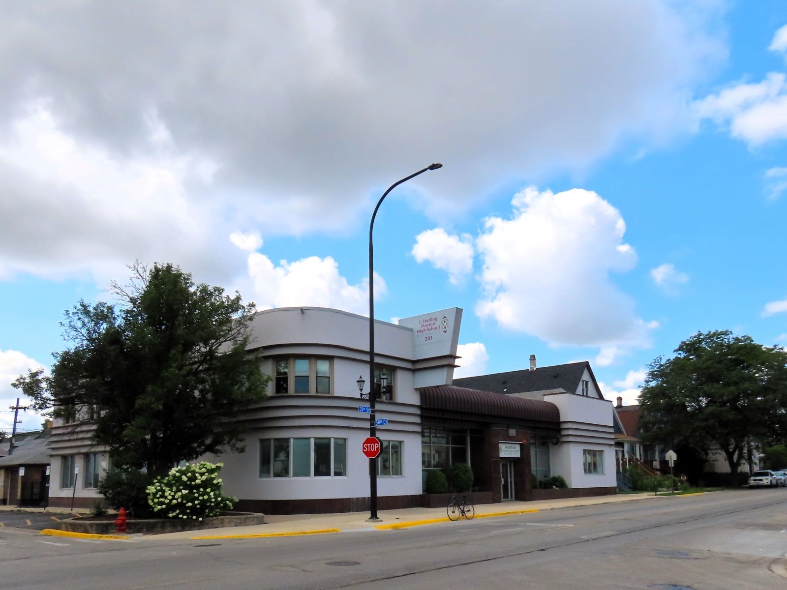 On a tree lined neighborhood street On a main street artery a tour bicycle is standing at front of a corner building with Streamline Art Deco styling.