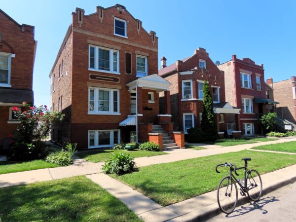 On a neighborhood street a tour bicycle is standing at front of early 1900s brown brick three and two flats.