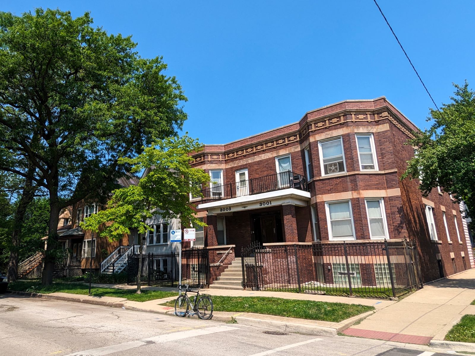 On a tree lined neighborhood street a tour bicycle is standing at front of an early 1900s two story brown brick two flat duplex.