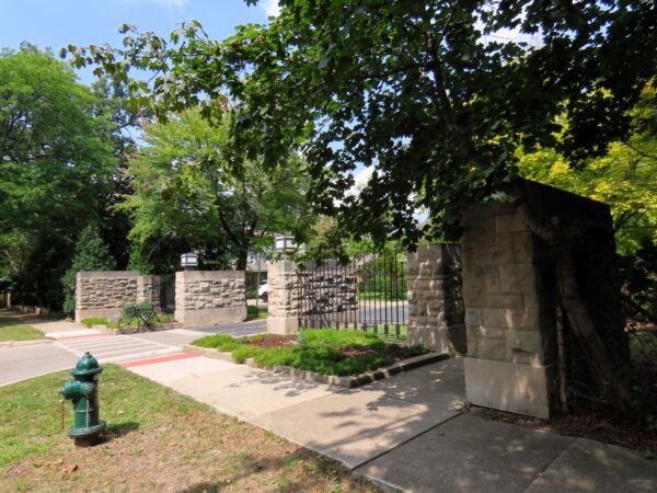 A tour bicycle leaning on the base of one of four rough stone gate plinths with two Prairie School lanterns at top.