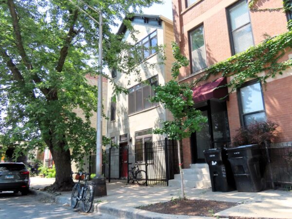 A tour bicycle standing at front of a modern sided early 1900s three flat under tree cover.