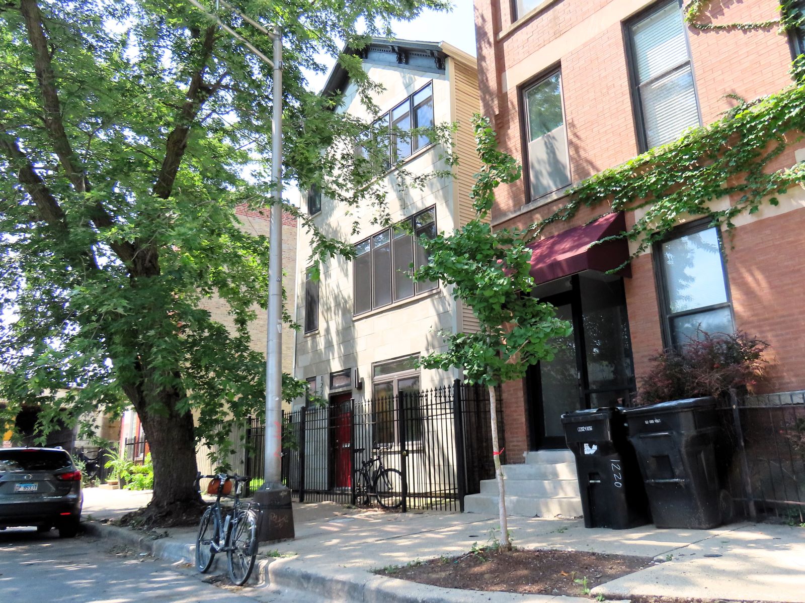 A tour bicycle standing at front of a modern sided early 1900s three flat under tree cover.