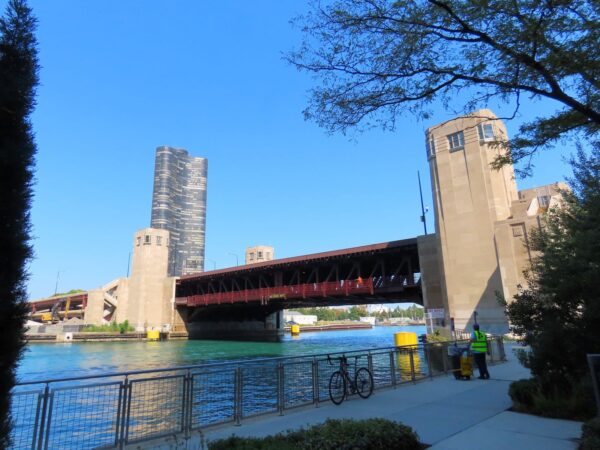 A tour bicycle leaning on the railing above the Chicago River with the massive Art Deco limestone and red painted steel Lake Shore Drive bridge.