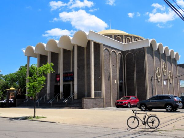 A tour bicycle standing near a dark brown brick and white Mid Century Modern Greek Orthodox large central dome church.