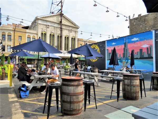 Four CBA riders sitting under a picnic table umbrella with a Classical Revival movie theater and bicycle themed mural in the background.