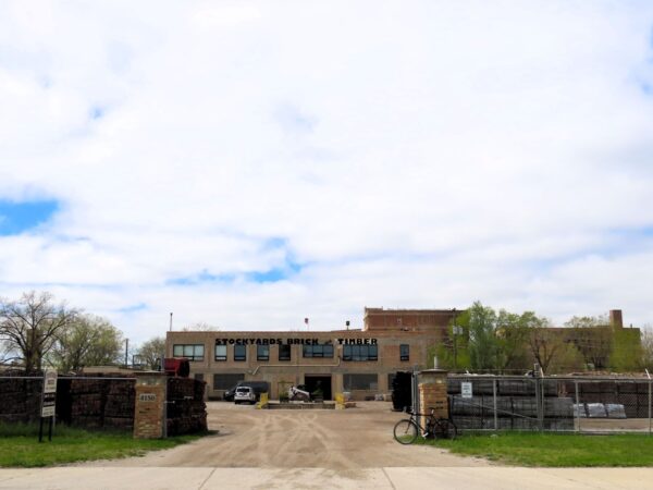 A tour bicycle leaning on the brick gate entrance of a two story brick business with wide dirt front yard.