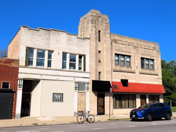 A tour bike standing at front of a two story limestone Art Deco former movie theater with small corner tower.