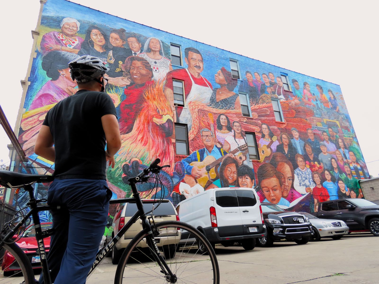 A CBA bike tour rider looking at a large mural of people done in the traditional Mexican style.