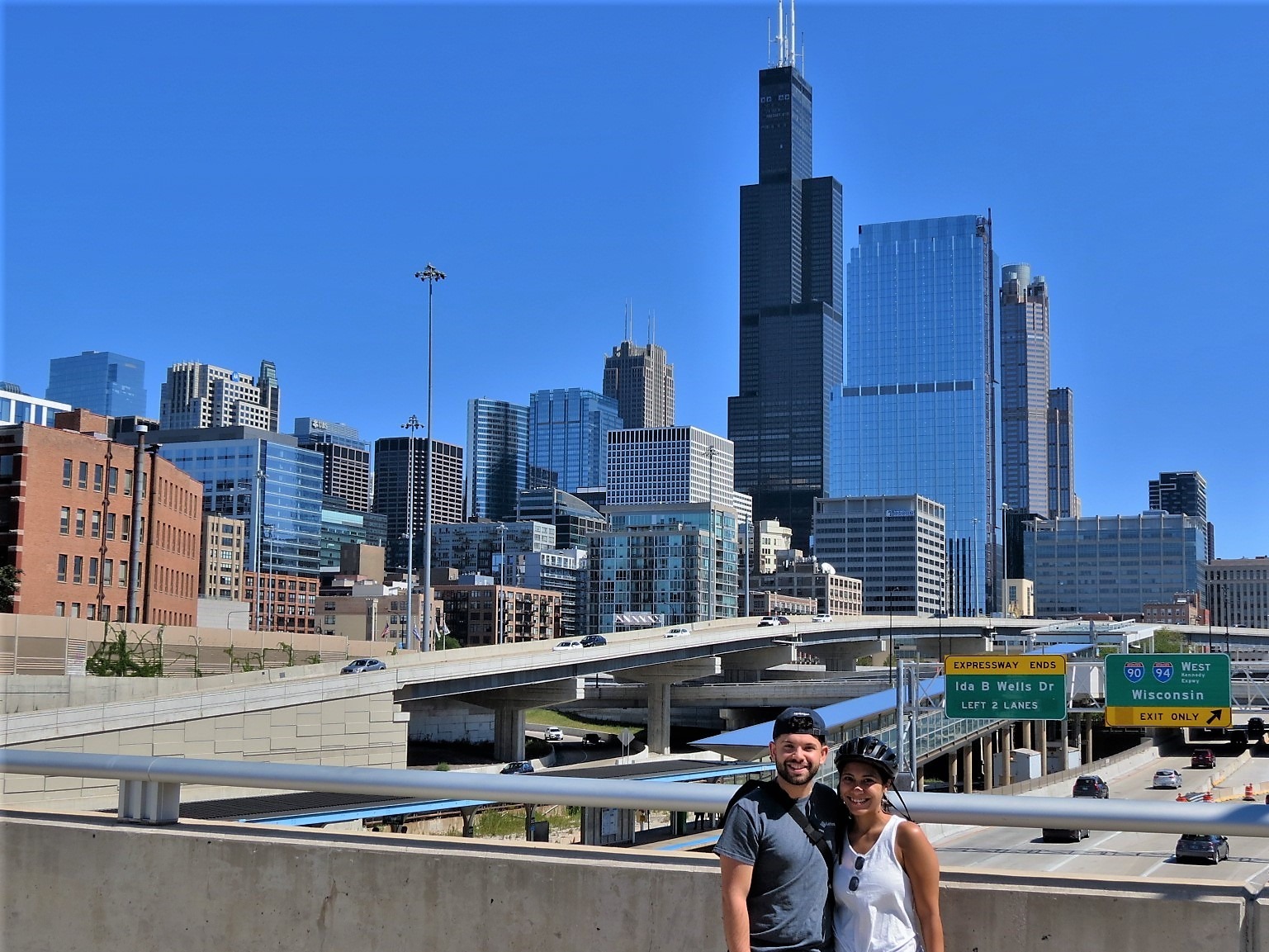 Two CBA bike tour riders smiling at the camera with the Chicago skyline including the Willis Tower behind