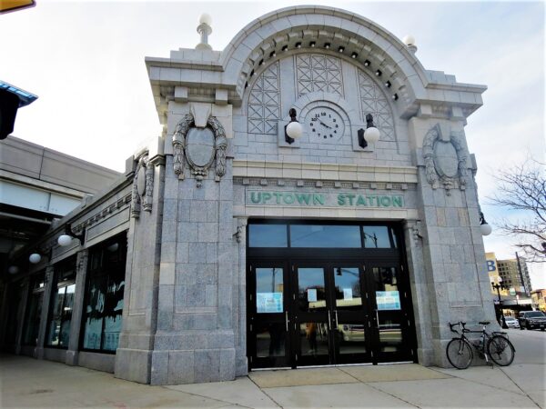 A tour bike leaning at the side of the entrance of a grey terra cotta one story corner Beaux Arts train station.