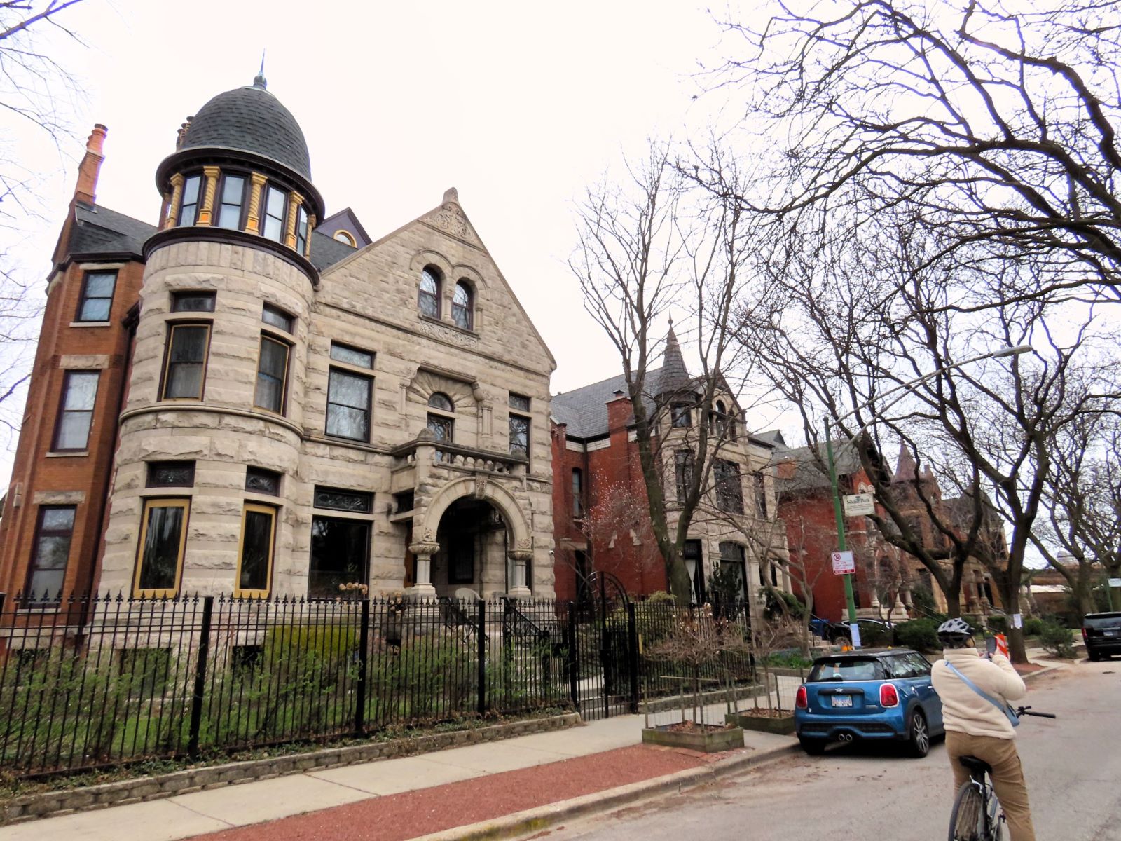 A CBA bike tour rider taking a picture of late 1800s Queen Anne homes under leafless trees.