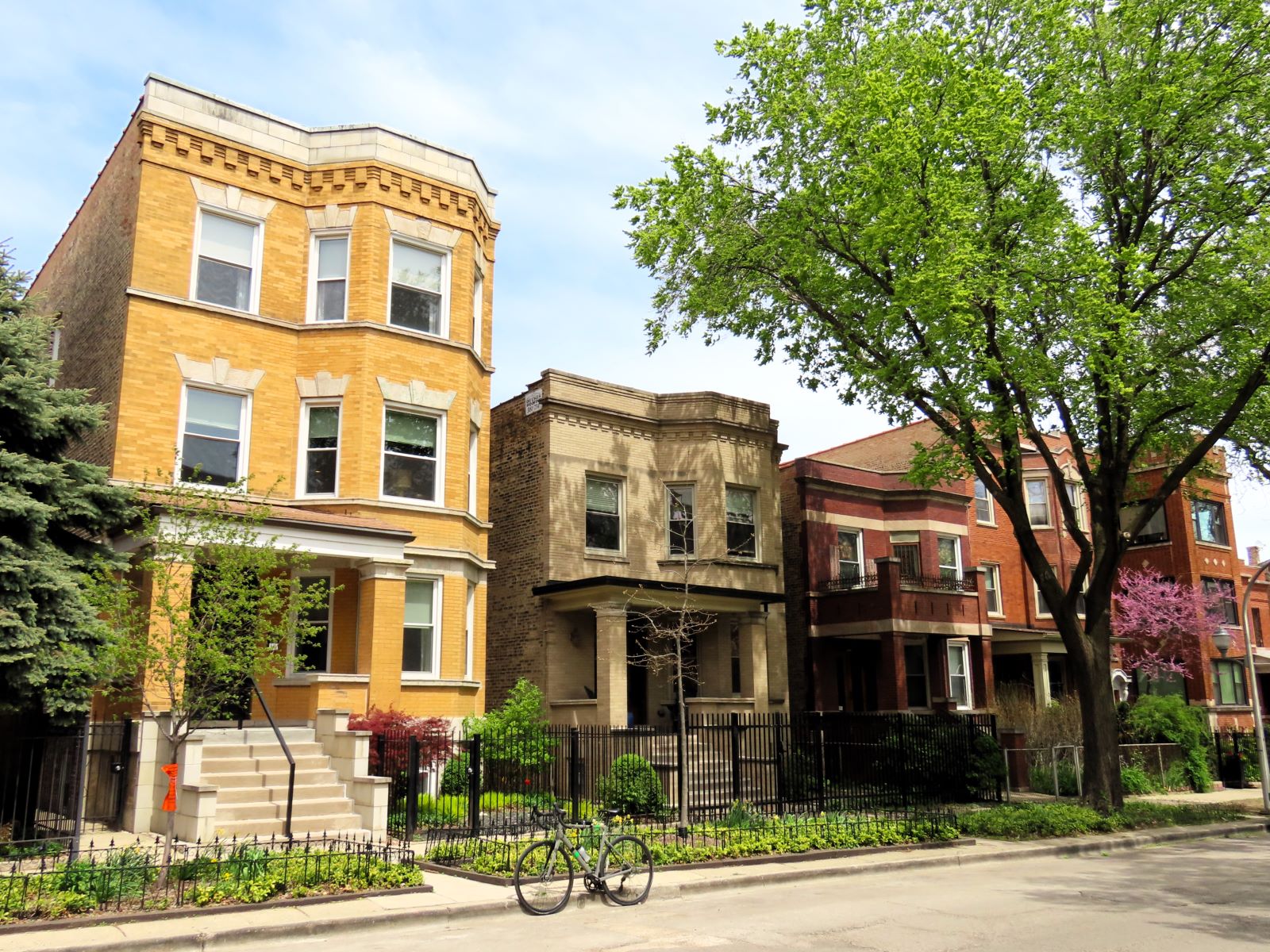 A tour bike standing at front of an early 1900s yellow brick three flat with shorter contemporary neighbors.