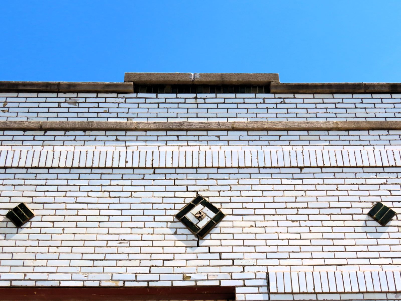 A white glazed brick building roofline with three green glazed brick square designs.