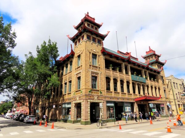 A tour bicycle standing at the corner of a three story terra cotta covered Chinese style public building with two pagoda like towers on the front corners.