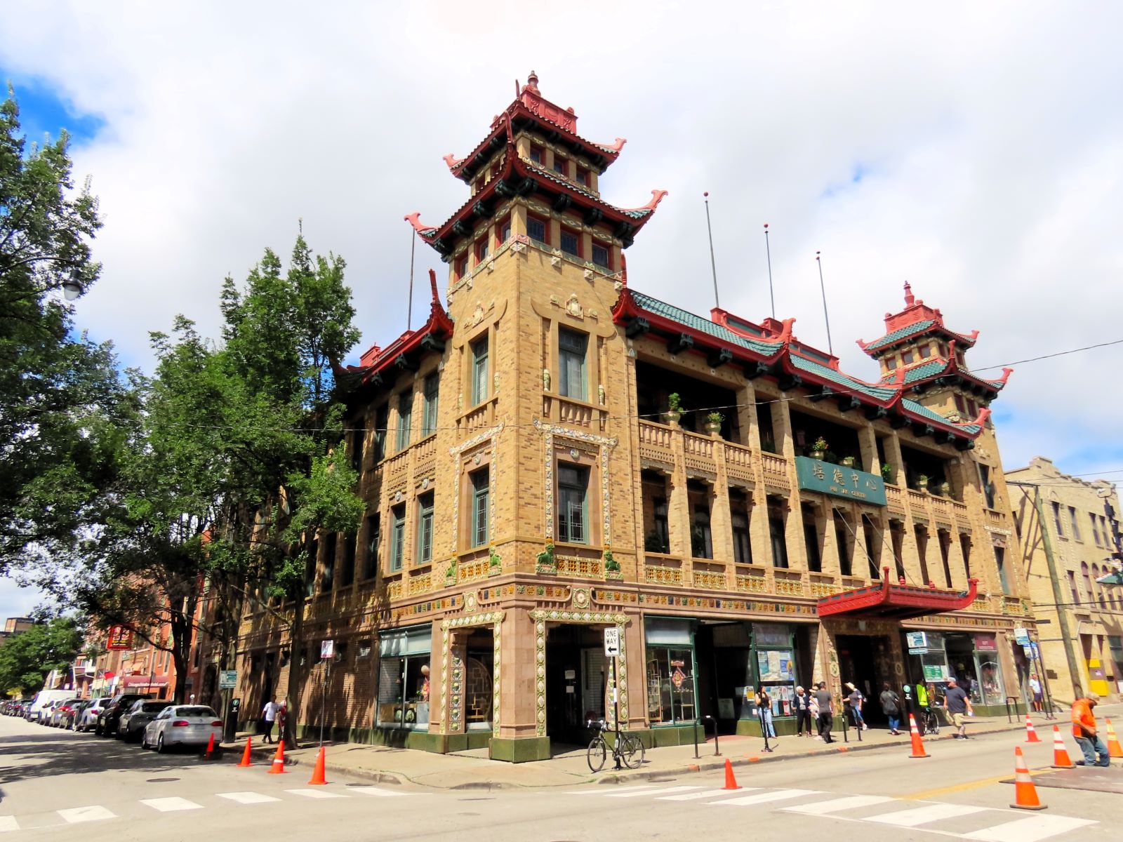A tour bicycle standing at the corner of a three story terra cotta covered Chinese style public building with two pagoda like towers on the front corners.