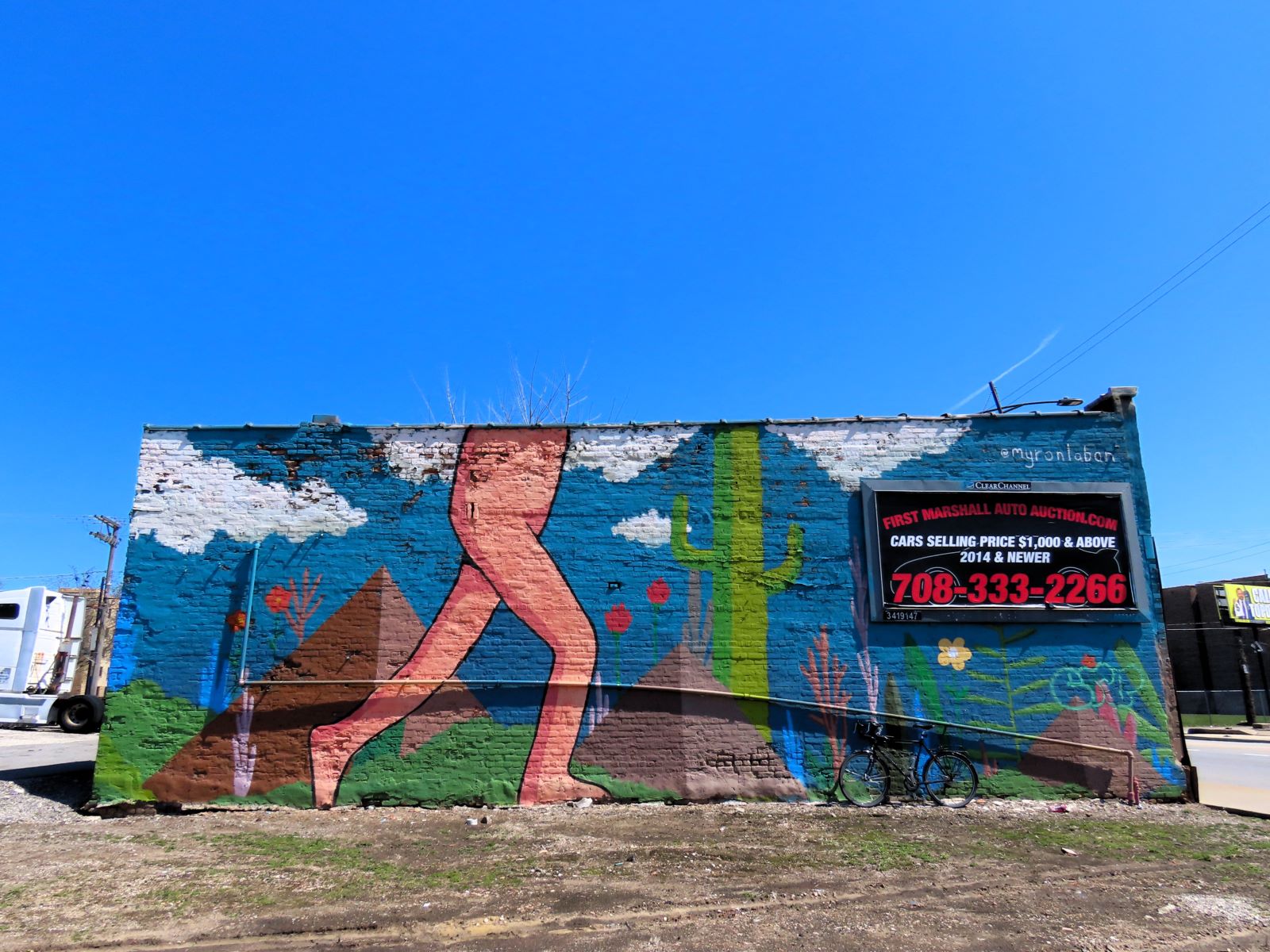 A tour bike leaning on a mural showing a smooth pink figure from the chest down walking through pyramids and cacti.