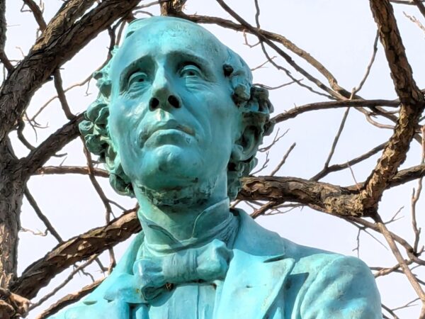 A closeup of a green copper head of Hans Christian Anderson in a bowtie.